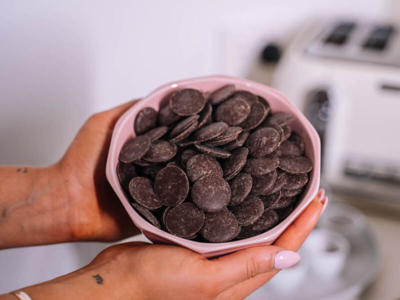 A pink bowl of chocolate buttons held by a person with pink nails 